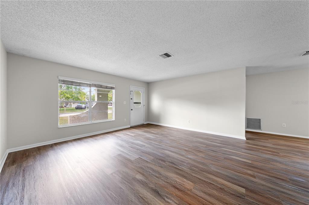 An empty living room features light gray walls, wood-look flooring, and a front entry door — 1501 VIRGINIA AVENUE, ST CLOUD, FL