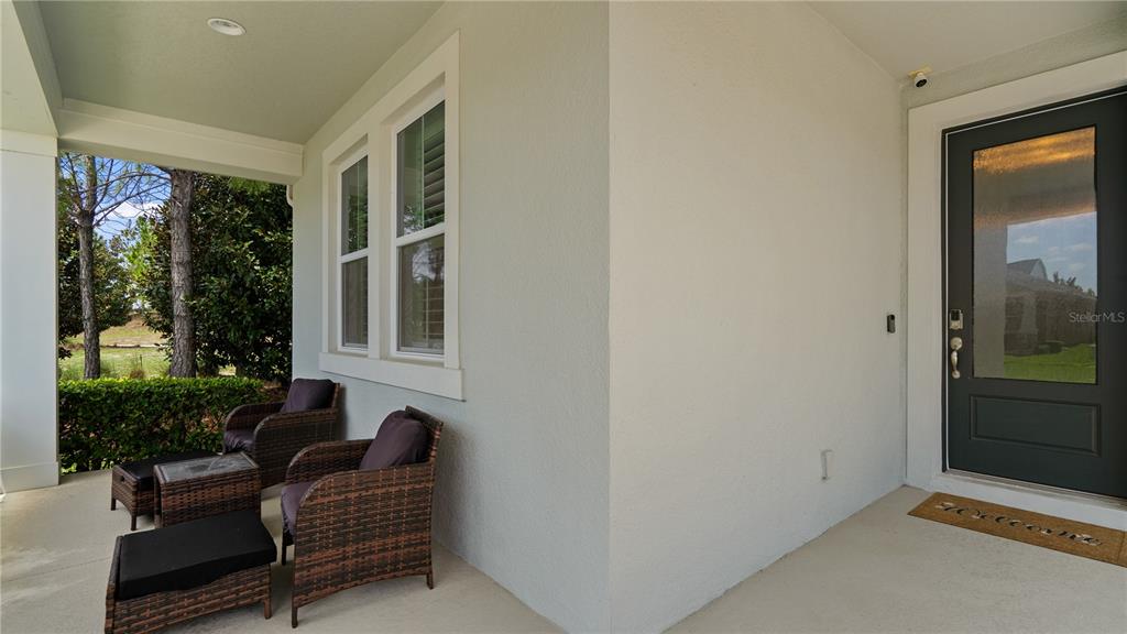 A covered front porch features two wicker chairs, a small table, and a dark door — 15395 SUGAR CITRUS DRIVE, WINTER GARDEN, FL