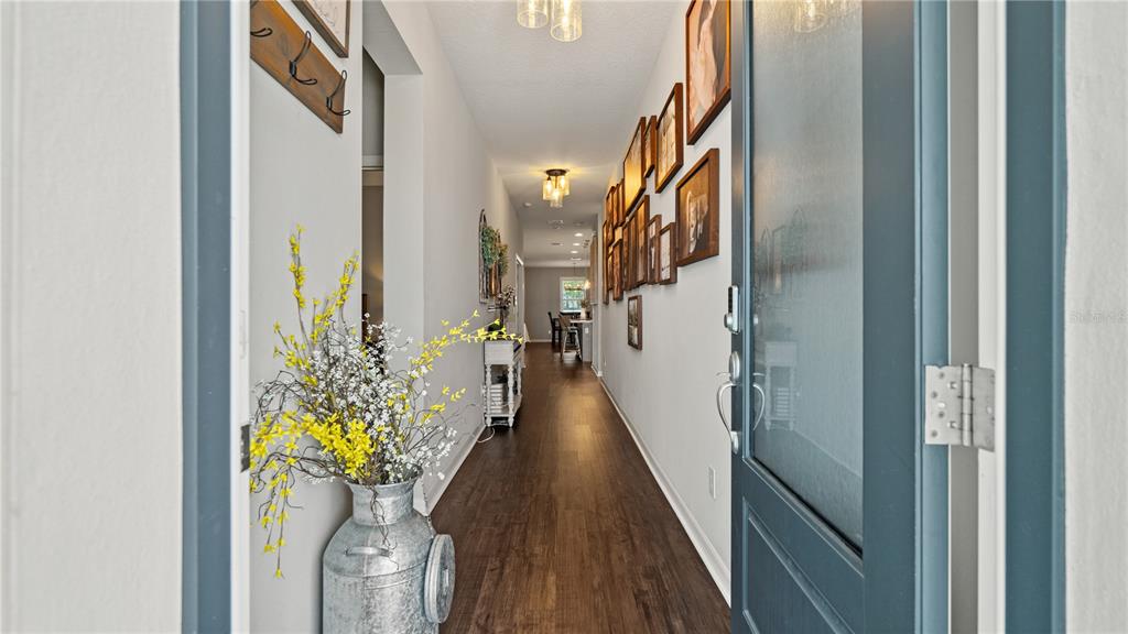 A long hallway with dark wood floors, a gallery wall, and a metal milk can planter — 15395 SUGAR CITRUS DRIVE, WINTER GARDEN, FL