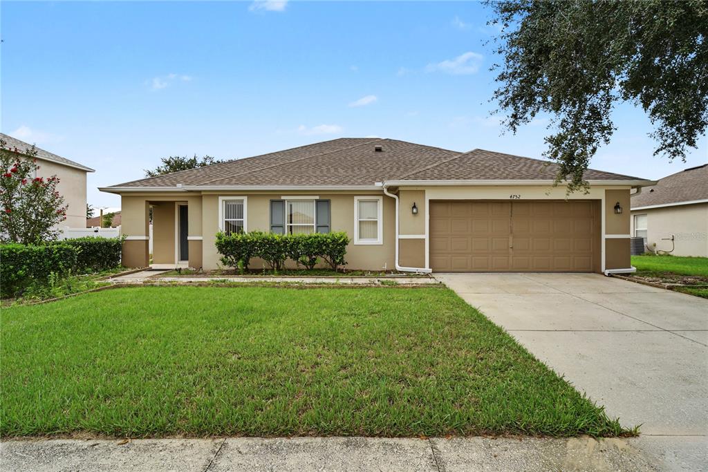 A single-story house with a tan stucco exterior, a brown roof, and a two-car garage — 4752 BARBADOS LOOP, CLERMONT, FL