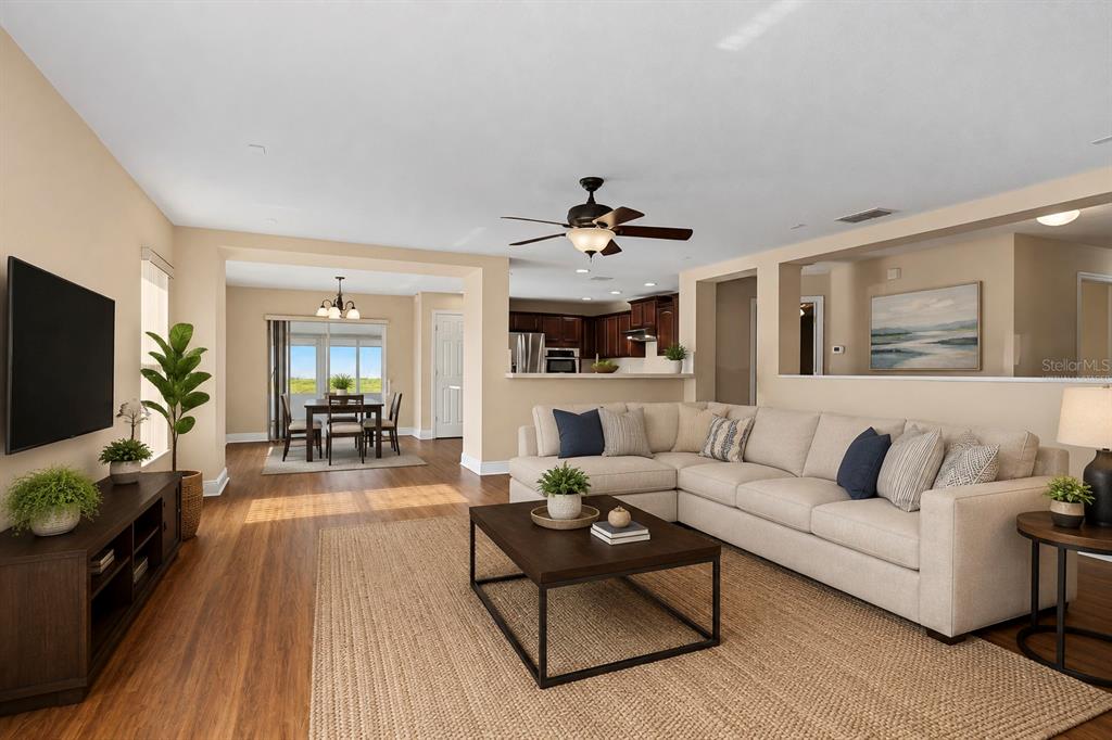 A living room with wood-look flooring, a sectional sofa, and an open kitchen beyond — 4752 BARBADOS LOOP, CLERMONT, FL