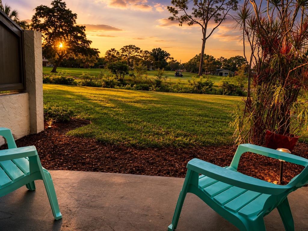 Two turquoise chairs sit on a concrete patio overlooking a grassy golf course at sunset — 2117 LAKEWOOD CLUB DRIVE S UNIT 7-N, ST PETERSBURG, FL