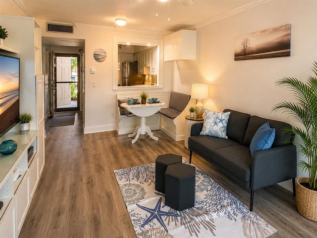 A living room features a dark sofa, a dining nook, and a television on wood flooring — 2117 LAKEWOOD CLUB DRIVE S UNIT 7-N, ST PETERSBURG, FL
