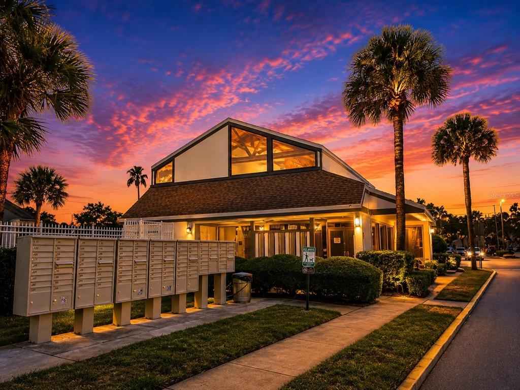 A community building exterior with a row of mailboxes and palm trees at sunset — 2117 LAKEWOOD CLUB DRIVE S UNIT 7-N, ST PETERSBURG, FL