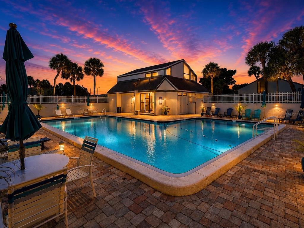 A swimming pool sits in front of a building at sunset with palm trees nearby — 2117 LAKEWOOD CLUB DRIVE S UNIT 7-N, ST PETERSBURG, FL