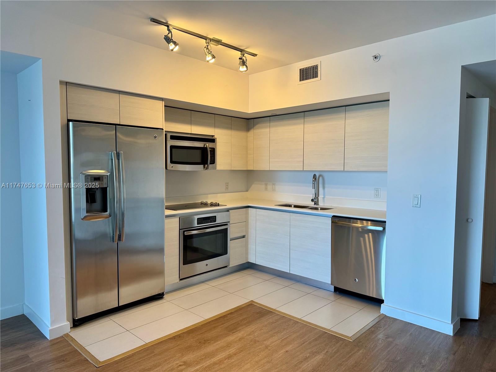 A modern kitchen features stainless steel appliances, light wood cabinetry, and white tile flooring — 4250 Biscayne Blvd # 1006, Miami FL 33137, MIAMI, FL