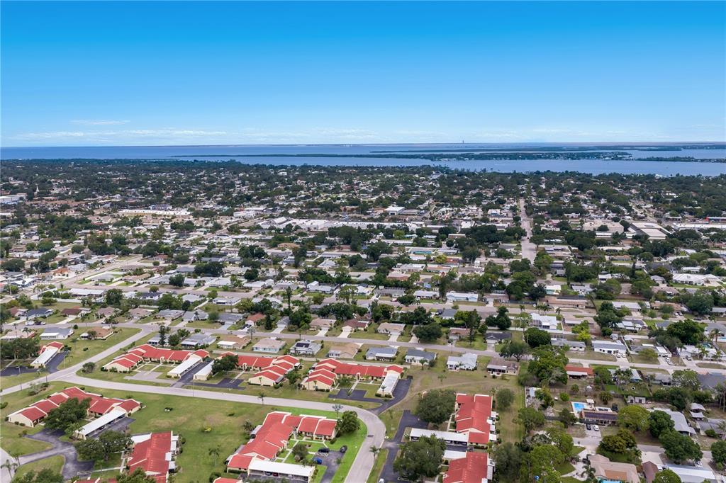 An aerial view shows a residential neighborhood with red-roofed buildings near a large body of water — 1208 56TH STREET W UNIT 1208, BRADENTON, FL