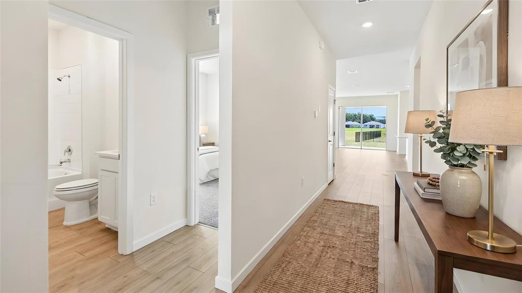 A hallway with light wood flooring leads past a bathroom and bedroom toward a living area — 3022 CANOPY OAK BOULEVARD, WILDWOOD, FL