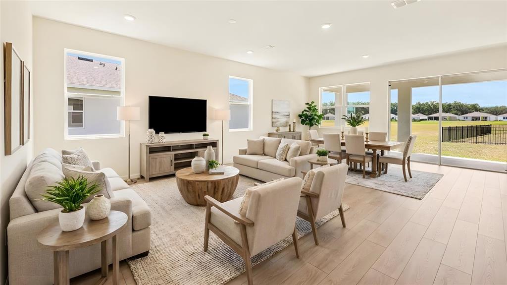 This open-concept living and dining area features light wood flooring and large sliding glass doors — 3022 CANOPY OAK BOULEVARD, WILDWOOD, FL