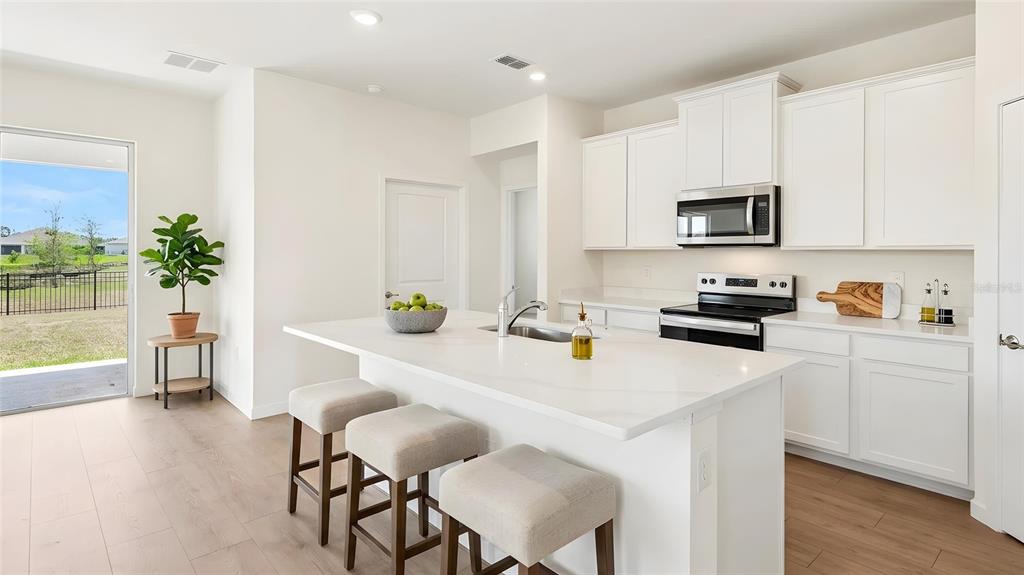 A bright kitchen features white cabinets, a quartz island with bar seating, and wood flooring — 3022 CANOPY OAK BOULEVARD, WILDWOOD, FL
