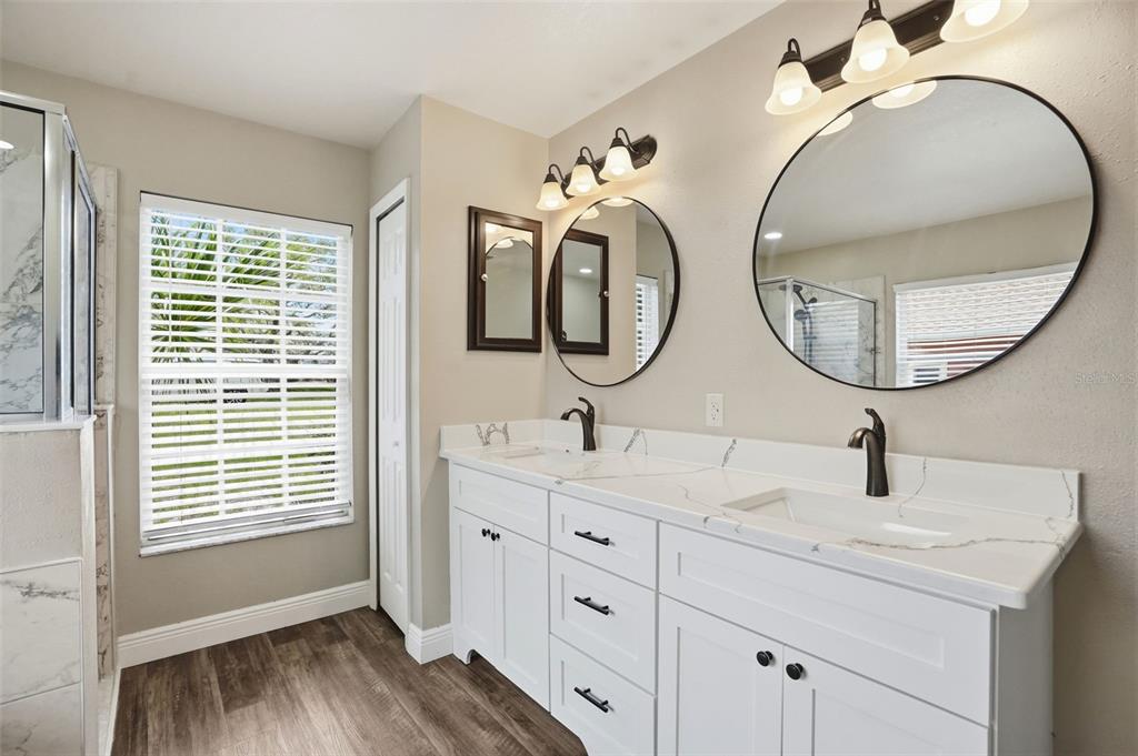 A bathroom features a double vanity with white cabinets, marble-look countertops, and two round mirrors — 10487 BRADFORD STREET, SPRING HILL, FL