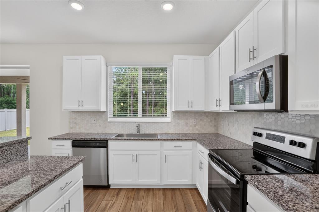A kitchen with white cabinets, granite countertops, stainless steel appliances, and wood-look flooring — 16420 WINDING PRESERVE CIRCLE, CLERMONT, FL