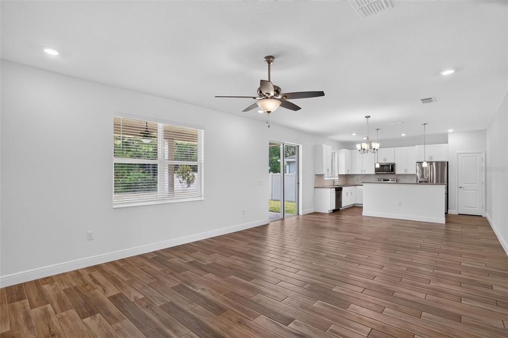 An open-concept living room and kitchen featuring wood-look tile flooring and white cabinetry — 16420 WINDING PRESERVE CIRCLE, CLERMONT, FL