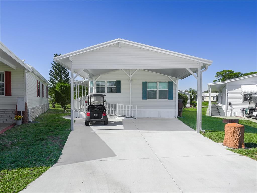 A white manufactured home features a large carport, a concrete driveway, and a wheelchair ramp — 43 RED QUILL CIRCLE, LAKE WALES, FL
