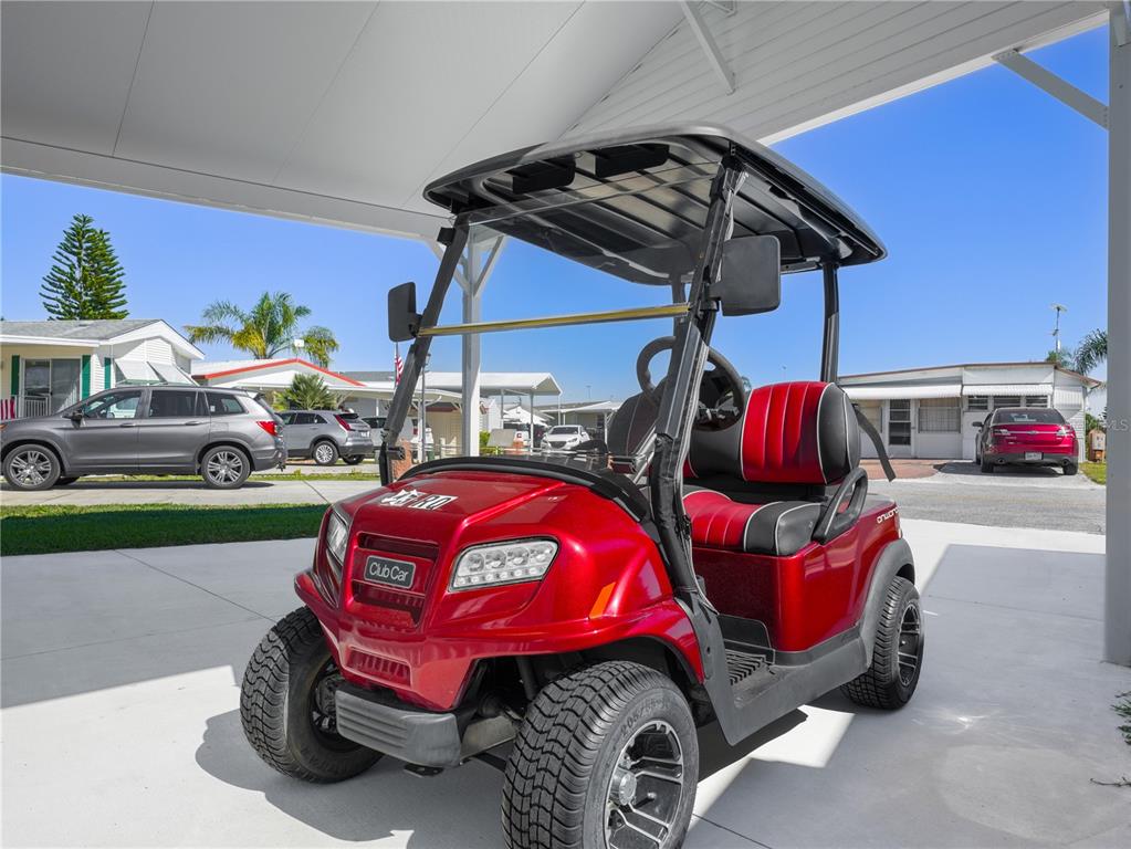 A red Club Car golf cart is parked under a carport in a residential area — 43 RED QUILL CIRCLE, LAKE WALES, FL