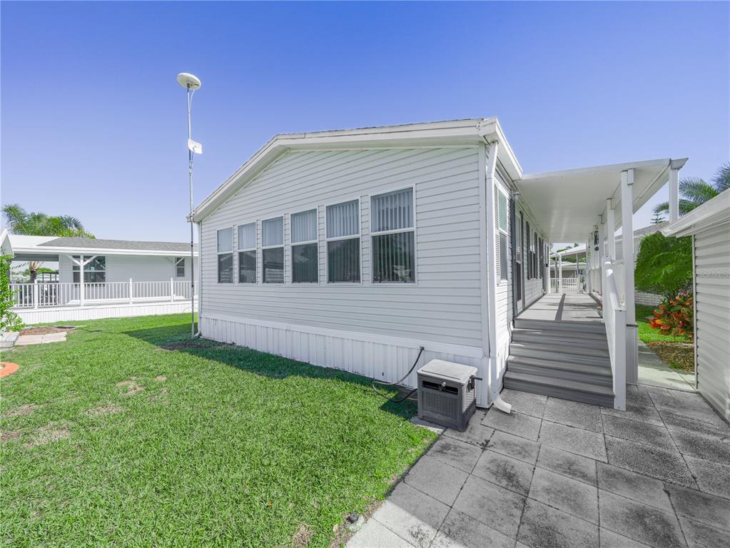 A light-colored mobile home with a covered porch, stairs, and a small lawn — 43 RED QUILL CIRCLE, LAKE WALES, FL