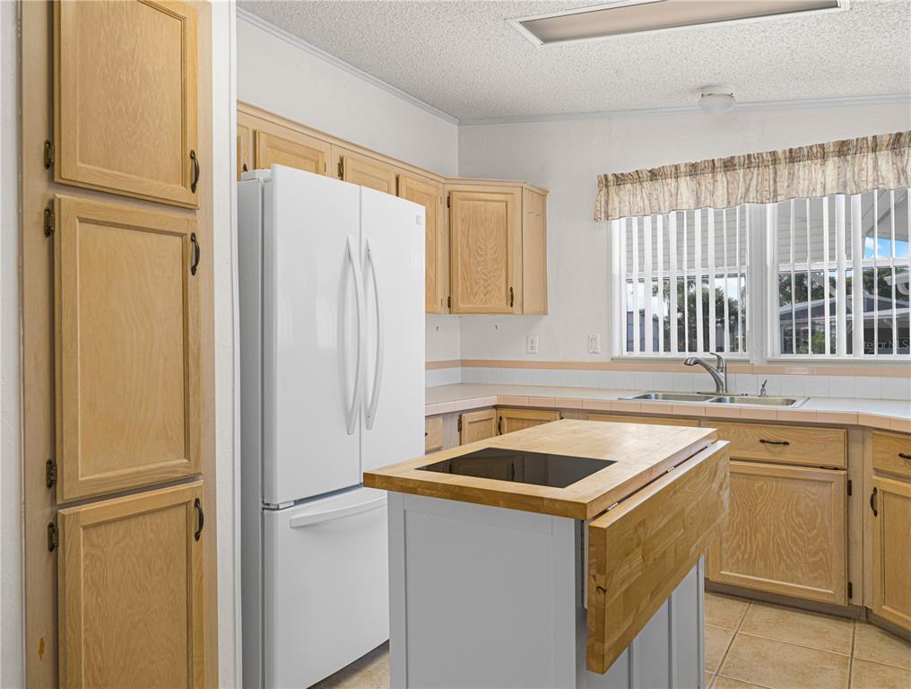 A kitchen features light wood cabinets, a white refrigerator, and a central island with a cooktop — 43 RED QUILL CIRCLE, LAKE WALES, FL