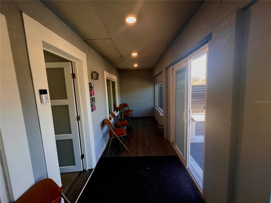 A covered porch features wood-look flooring, a black entry mat, sliding glass doors, and folding chairs — 5827 E COLUMBUS DRIVE, TAMPA, FL
