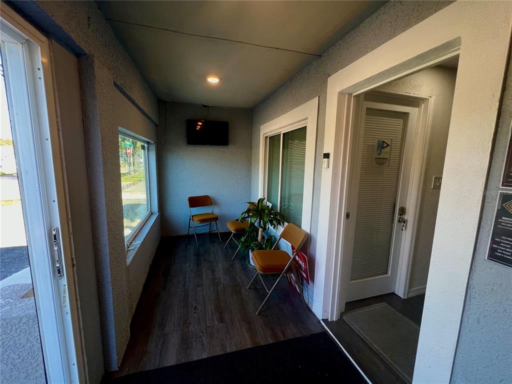 A small waiting area features wood-look flooring, two folding chairs, a plant, and a television — 5827 E COLUMBUS DRIVE, TAMPA, FL