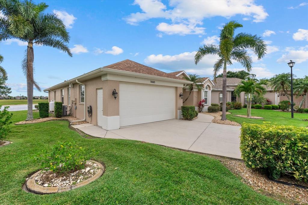 A tan single-story house with a two-car garage and palm trees in the front yard — 5665 RIVIERA COURT, NORTH PORT, FL