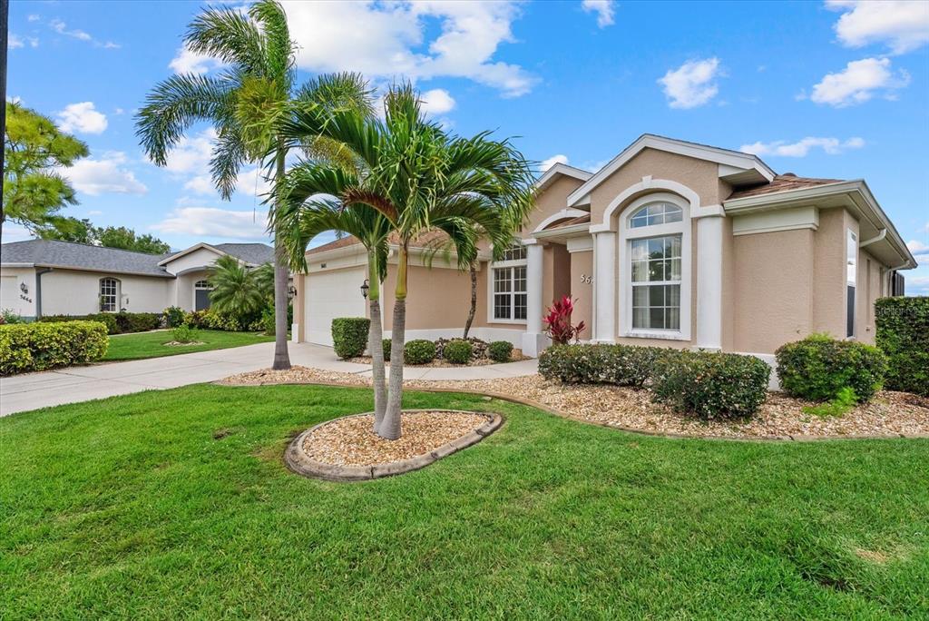 A tan single-story house with a palm tree in the front yard under a blue sky — 5665 RIVIERA COURT, NORTH PORT, FL