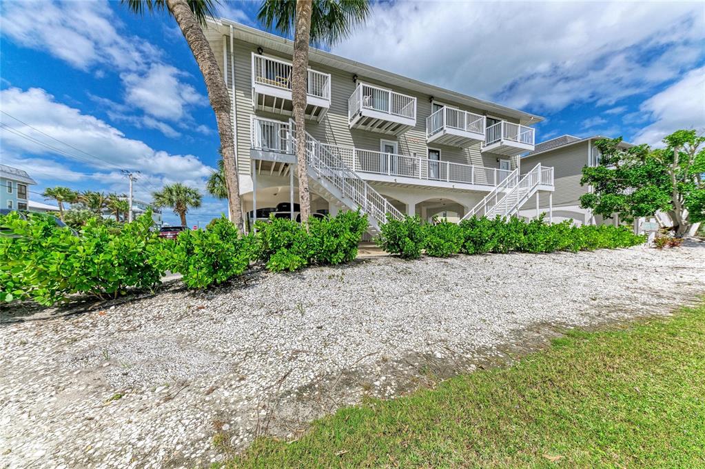 A multi-story coastal house features elevated balconies, white railings, and a gravel yard with landscaping — 3400 6TH AVENUE UNIT 6, HOLMES BEACH, FL