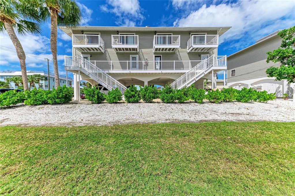 A two-story elevated house with white railings, stairs, and green siding sits above a parking area — 3400 6TH AVENUE UNIT 6, HOLMES BEACH, FL