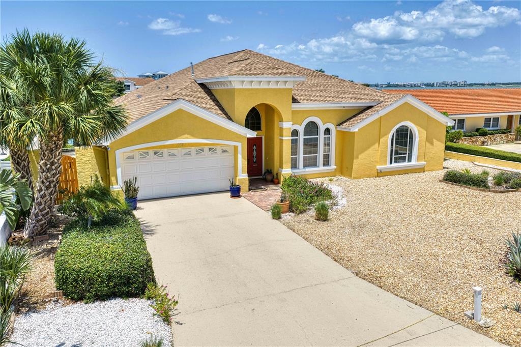 A yellow single-story house features a two-car garage, arched windows, and a gravel front yard — 115 ALETA DRIVE, BELLEAIR BEACH, FL