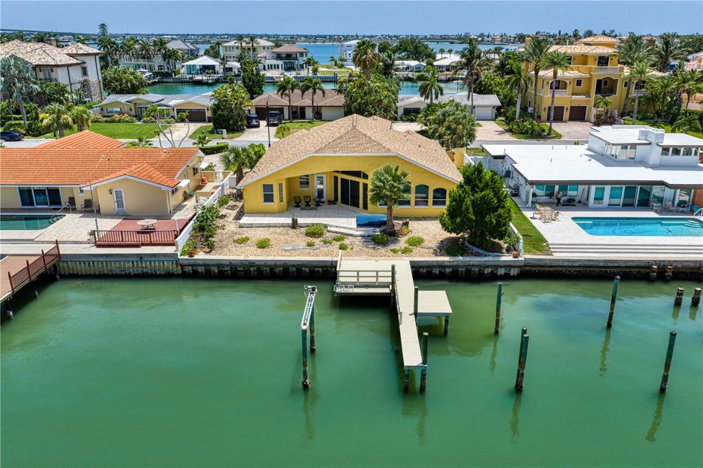An aerial view of a yellow waterfront house with a private dock and swimming pool — 115 ALETA DRIVE, BELLEAIR BEACH, FL