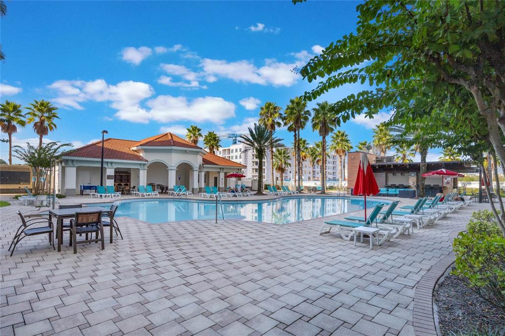 A swimming pool area with lounge chairs, tables, and a clubhouse under a blue sky — 7395 UNIVERSAL BOULEVARD UNIT 906, ORLANDO, FL