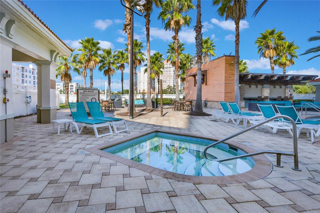 A rectangular hot tub sits on a paved patio surrounded by lounge chairs and palm trees — 7395 UNIVERSAL BOULEVARD UNIT 906, ORLANDO, FL