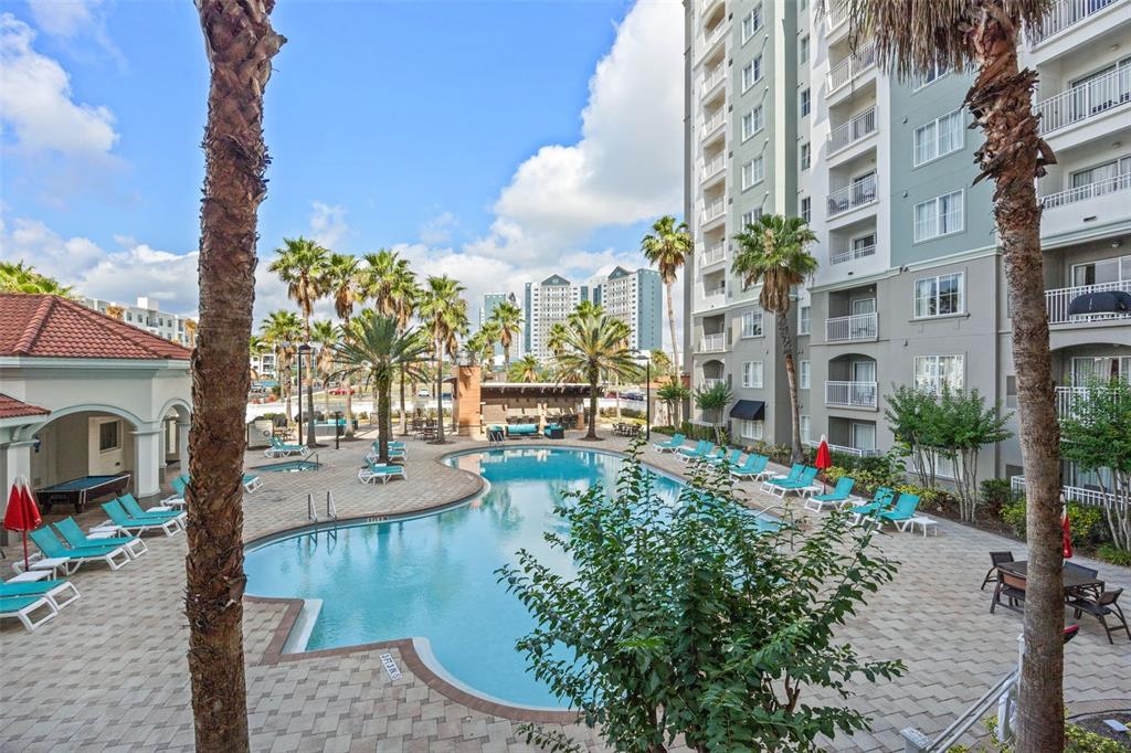 An outdoor swimming pool surrounded by lounge chairs, palm trees, and a multi-story apartment building — 7395 UNIVERSAL BOULEVARD UNIT 906, ORLANDO, FL