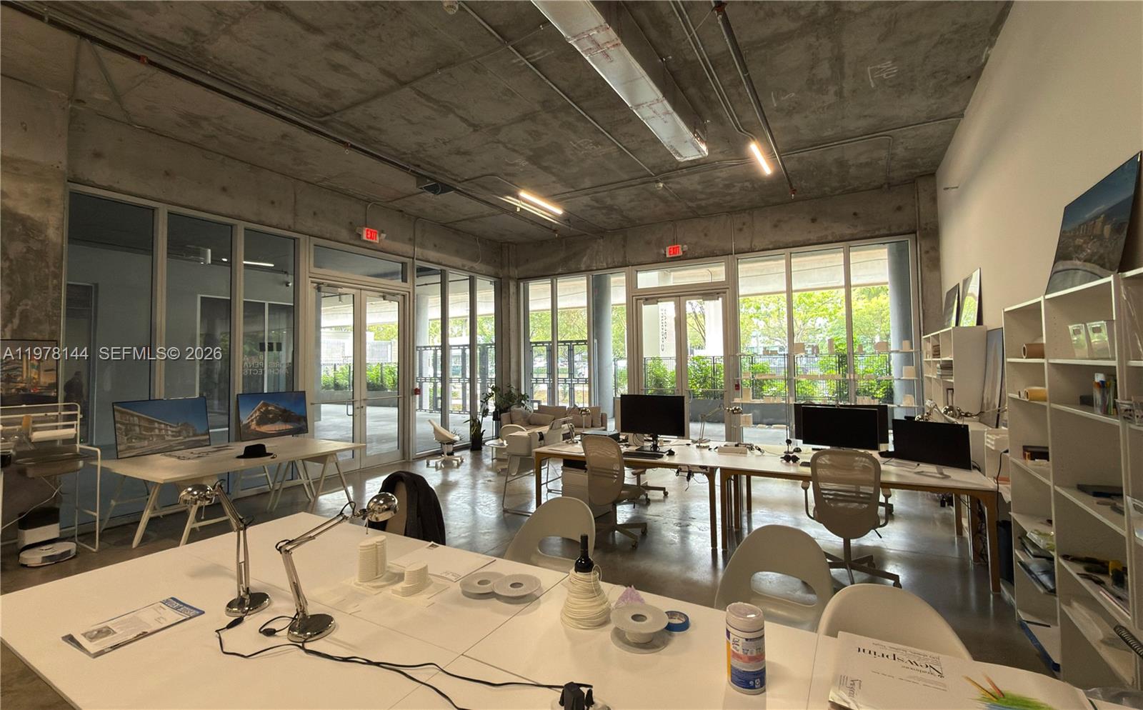 A modern office space features concrete ceilings, floor-to-ceiling windows, and multiple workstations — 2900 SW 28th Ln # C5, Miami FL 33133, MIAMI, FL
