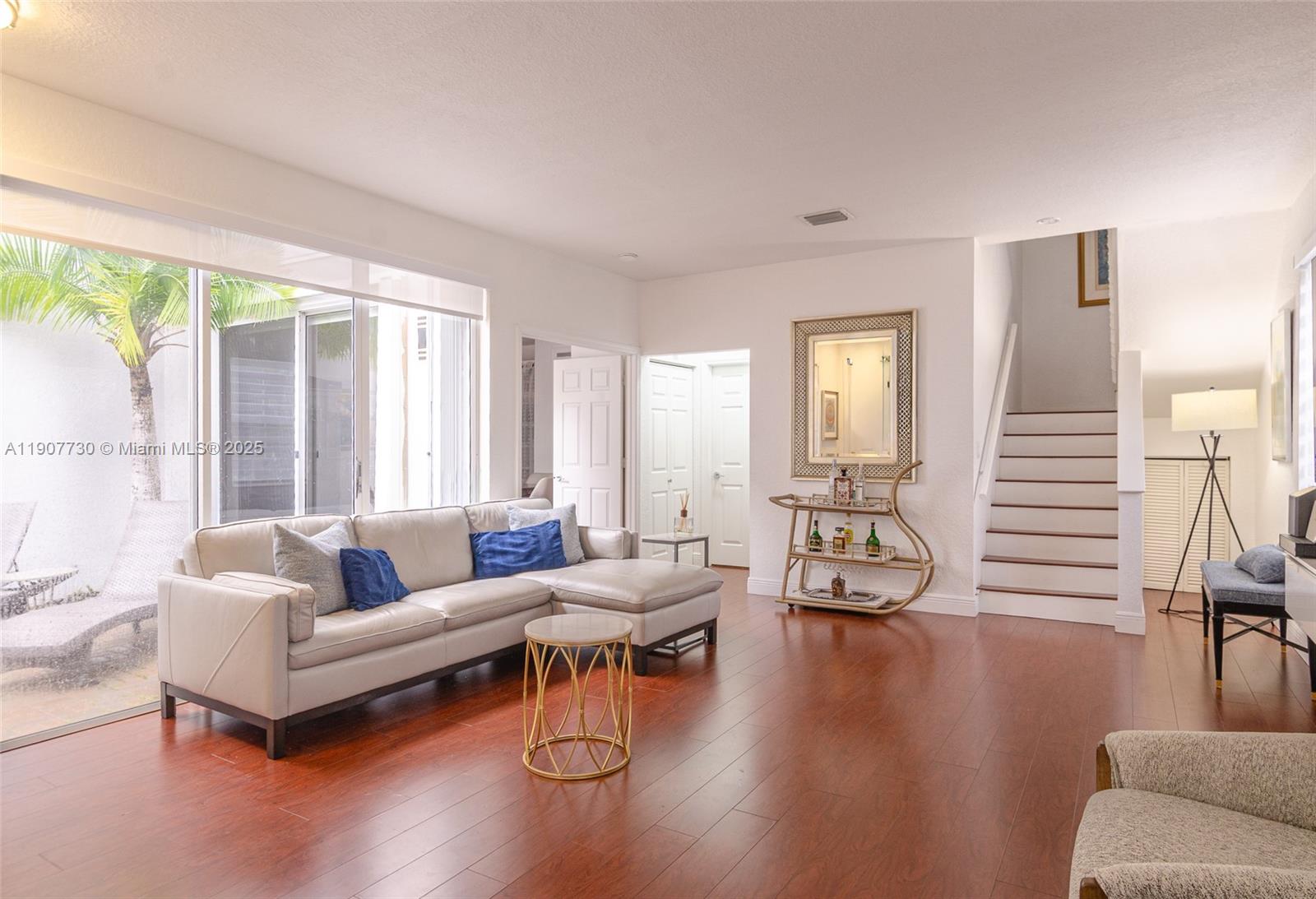 A living room features a light-colored sectional sofa, hardwood floors, and a staircase — 1115 Cherrypalm, Hollywood FL 33019, HOLLYWOOD, FL