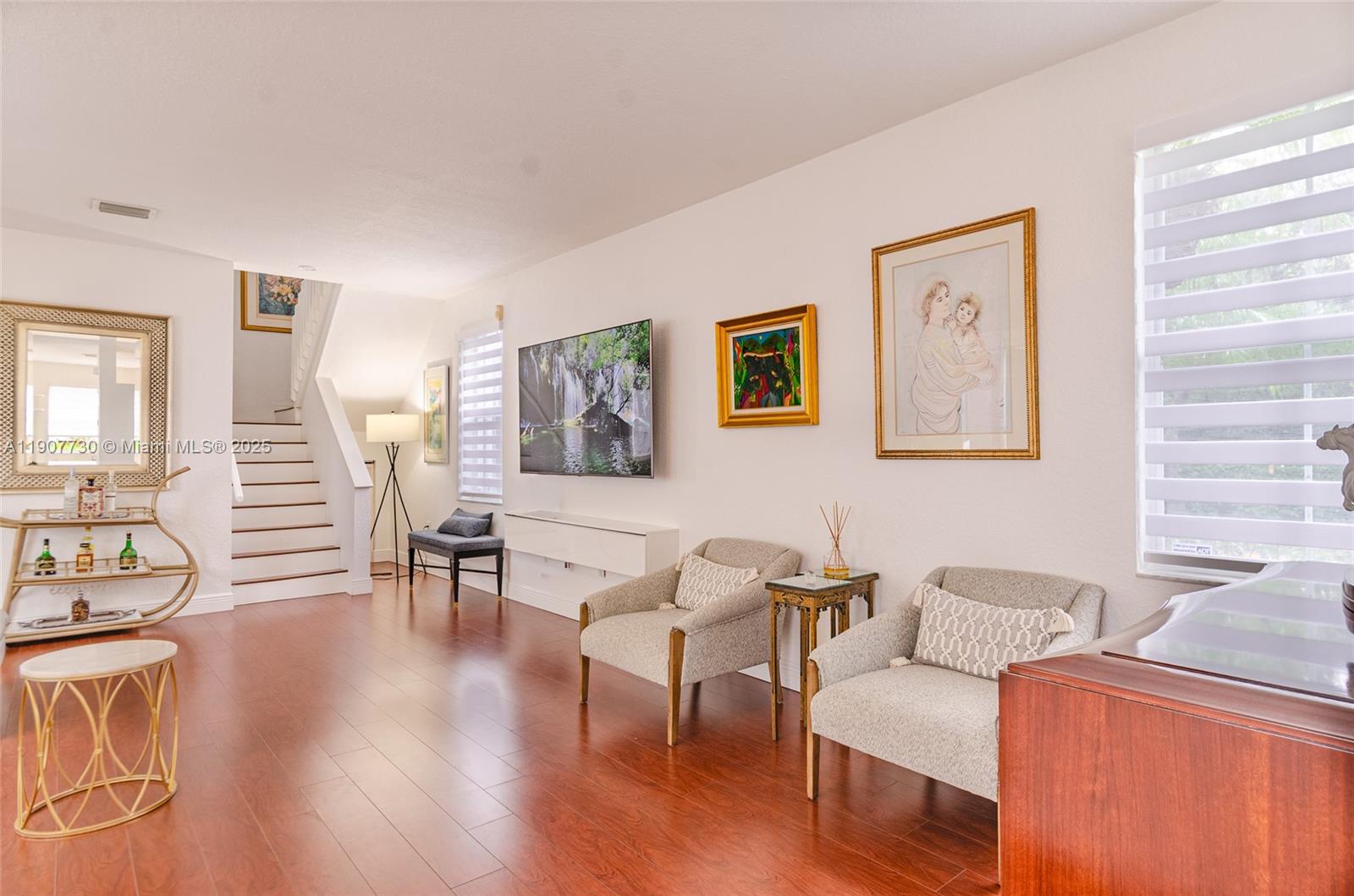 A living room features hardwood floors, two armchairs, a wall-mounted television, and a staircase — 1115 Cherrypalm, Hollywood FL 33019, HOLLYWOOD, FL