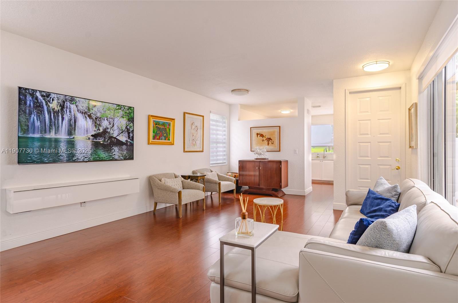 A living room features hardwood floors, a wall-mounted television, and a white leather sofa — 1115 Cherrypalm, Hollywood FL 33019, HOLLYWOOD, FL