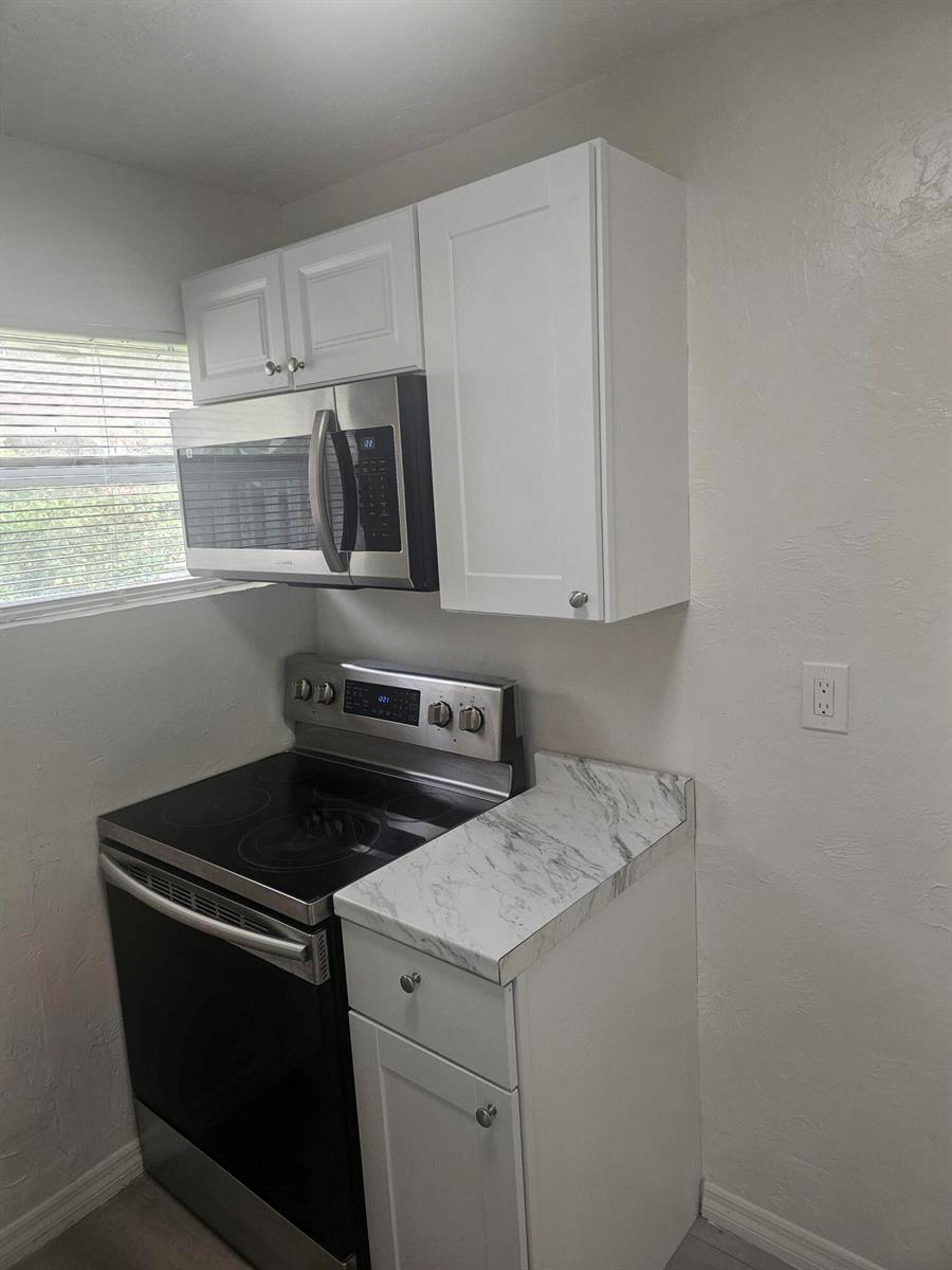 A kitchen features white cabinets, a stainless steel microwave, a glass-top stove, and marble-look countertops — 505 NW 16th Avenue, Pompano Beach FL 33069, POMPANO BEACH, FL