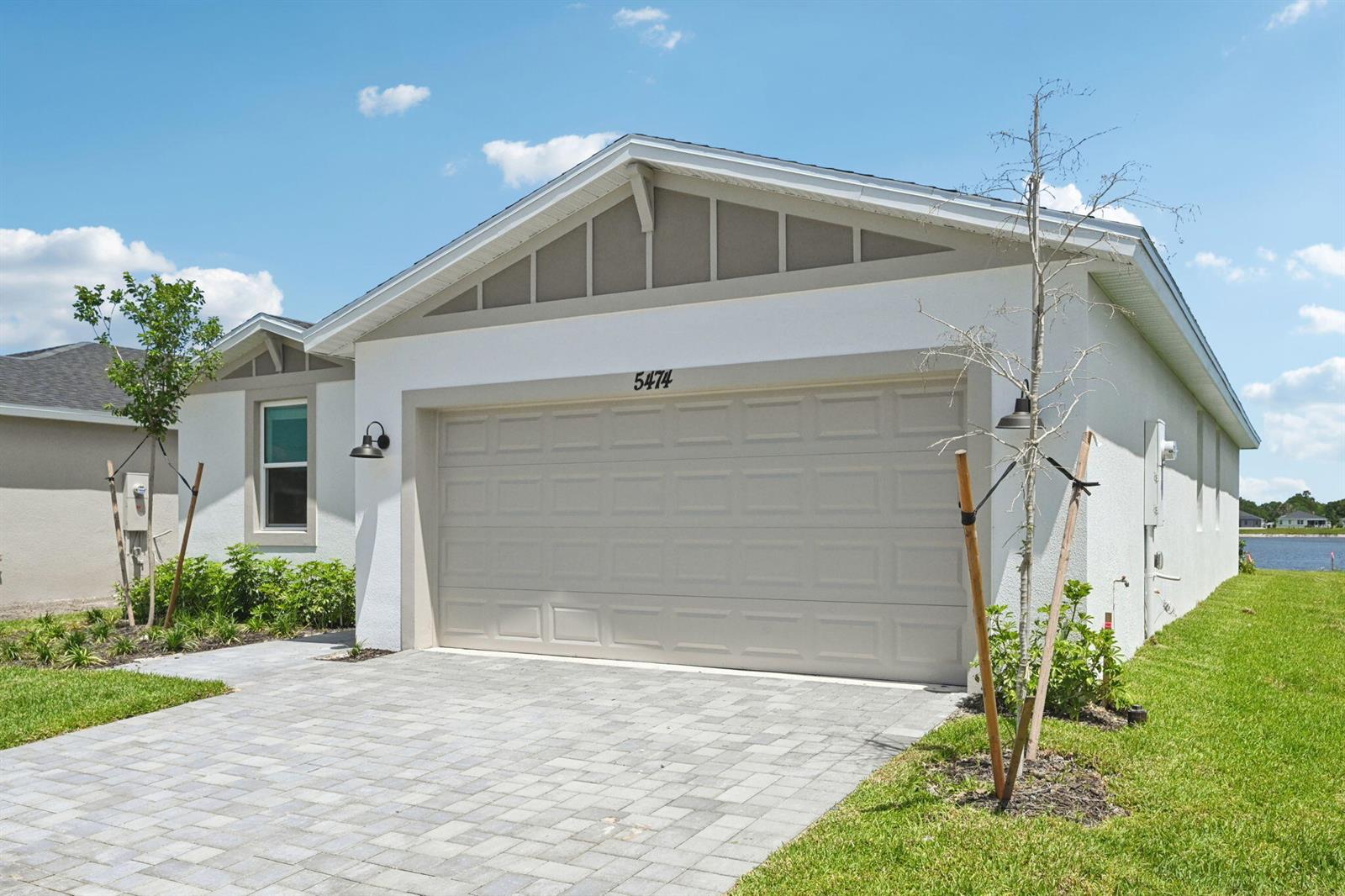 A single-story house exterior features a beige garage door, light-colored stucco walls, and a paver driveway — 5474 Hampton Park Circle, Vero Beach FL 32966, VERO BEACH, FL