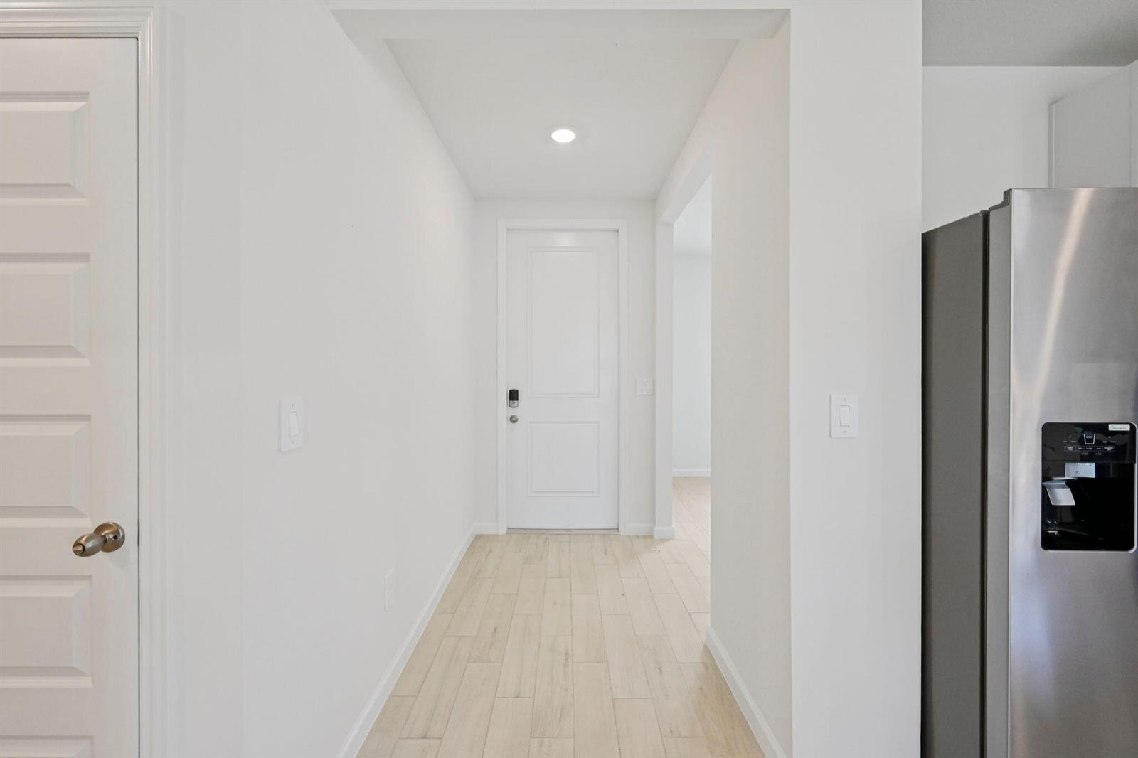 A hallway with light wood-look tile flooring leads to a white door — 5474 Hampton Park Circle, Vero Beach FL 32966, VERO BEACH, FL