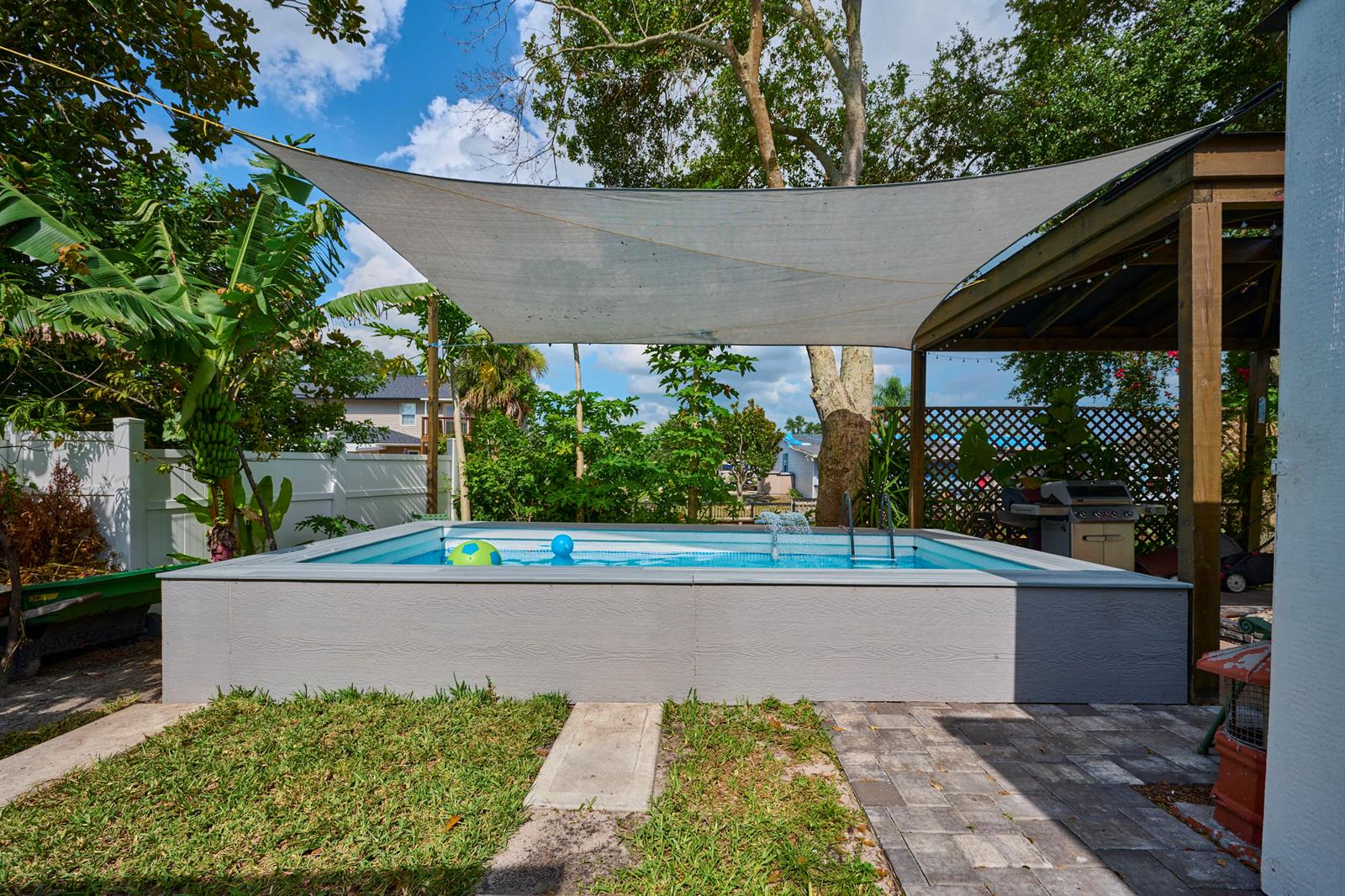 An above-ground swimming pool with a shade sail sits in a backyard with landscaping — 441 Spoonbill Court, FL 34739, FL