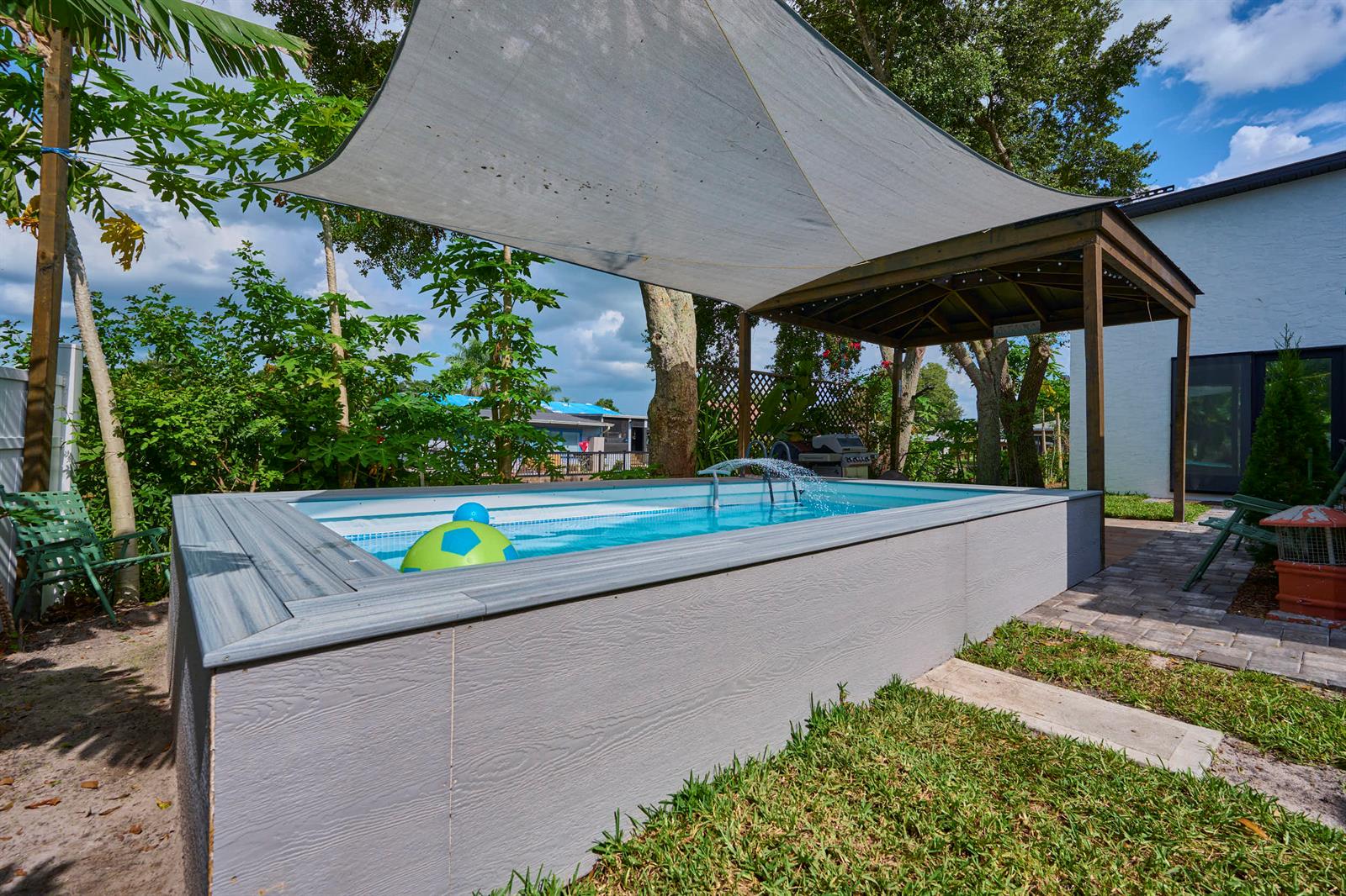 An above-ground rectangular swimming pool with a shade sail and wooden pergola in a backyard — 441 Spoonbill Court, FL 34739, FL