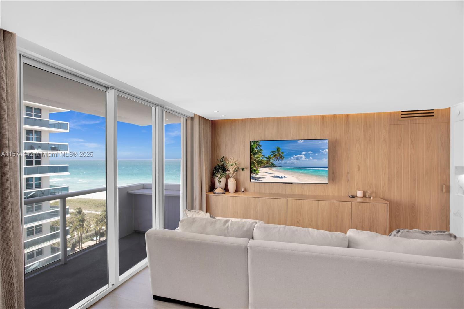 A living room features a wood-paneled wall, a mounted television, and a balcony overlooking the ocean — 9195 Collins Ave # 903, Surfside FL 33154, SURFSIDE, FL