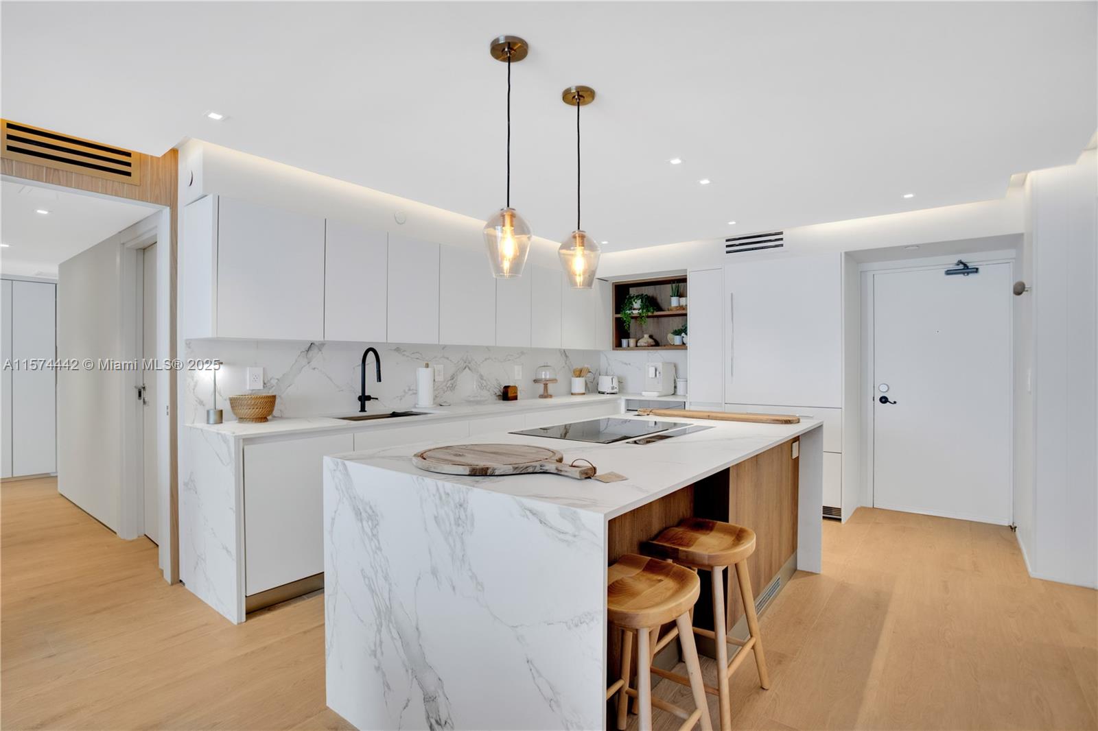 A modern kitchen features white cabinetry, marble countertops, a central island, and light wood flooring — 9195 Collins Ave # 903, Surfside FL 33154, SURFSIDE, FL