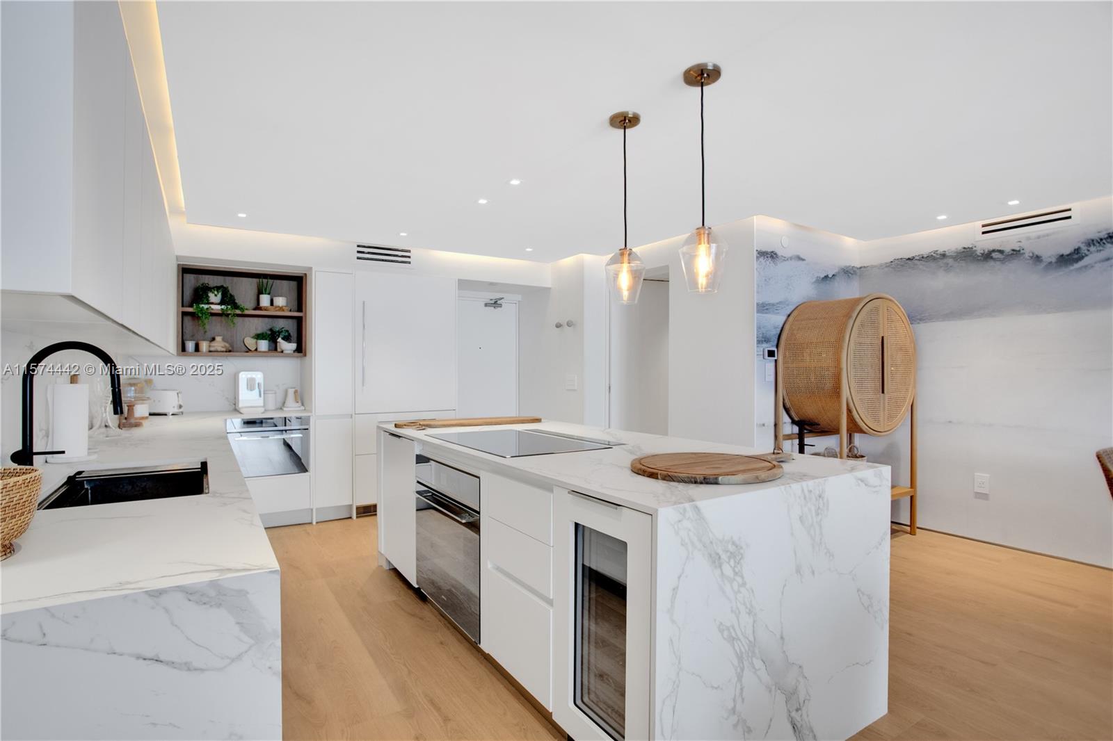 A modern kitchen features white marble countertops, light wood flooring, and a central island — 9195 Collins Ave # 903, Surfside FL 33154, SURFSIDE, FL