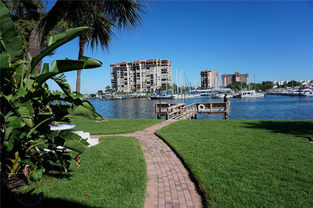 A brick walkway leads through a grassy lawn toward a wooden dock on the water — 9715 HARRELL AVENUE UNIT 14, TREASURE ISLAND, FL