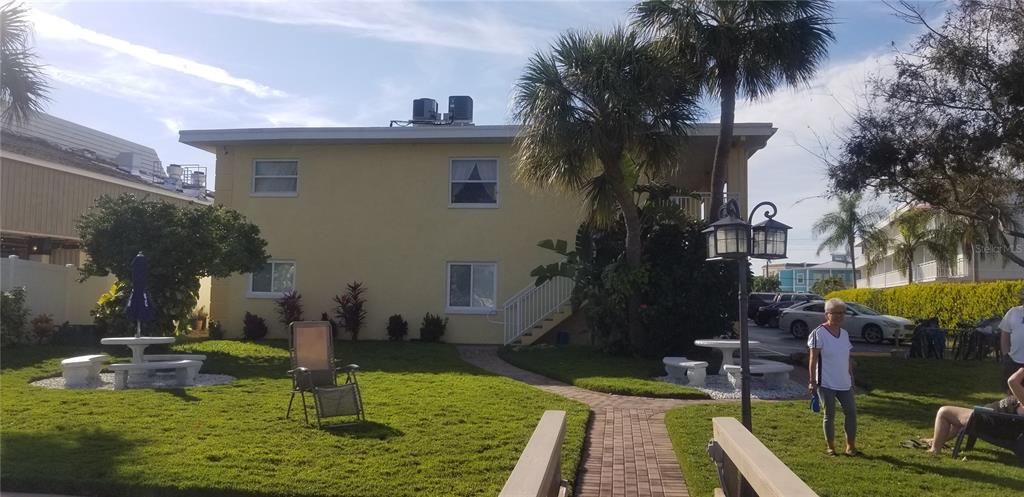 A two-story yellow building with a grassy yard, outdoor seating, and palm trees — 9715 HARRELL AVENUE UNIT 14, TREASURE ISLAND, FL