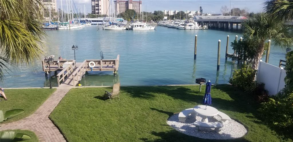 A grassy backyard features a picnic table, a wooden dock, and a view of boats — 9715 HARRELL AVENUE UNIT 14, TREASURE ISLAND, FL