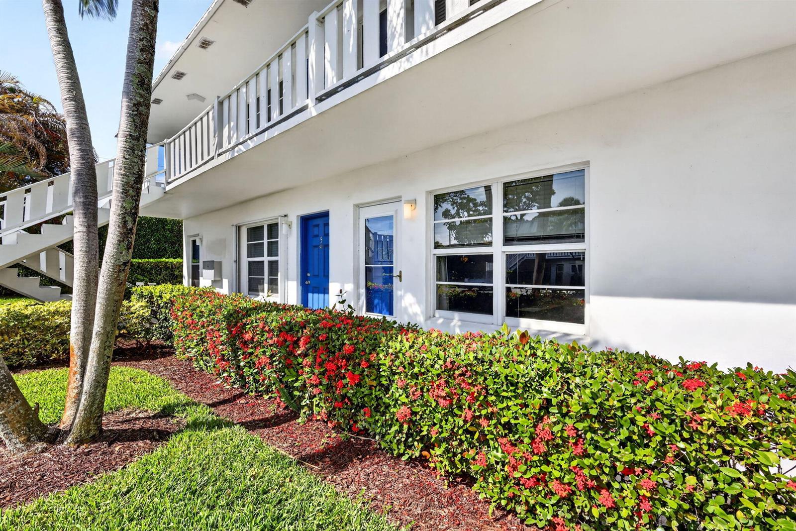 A two-story white apartment building features a blue door, large windows, and red-flowering hedges — 2929 SE Ocean Boulevard # M4, Stuart FL 34996, STUART, FL