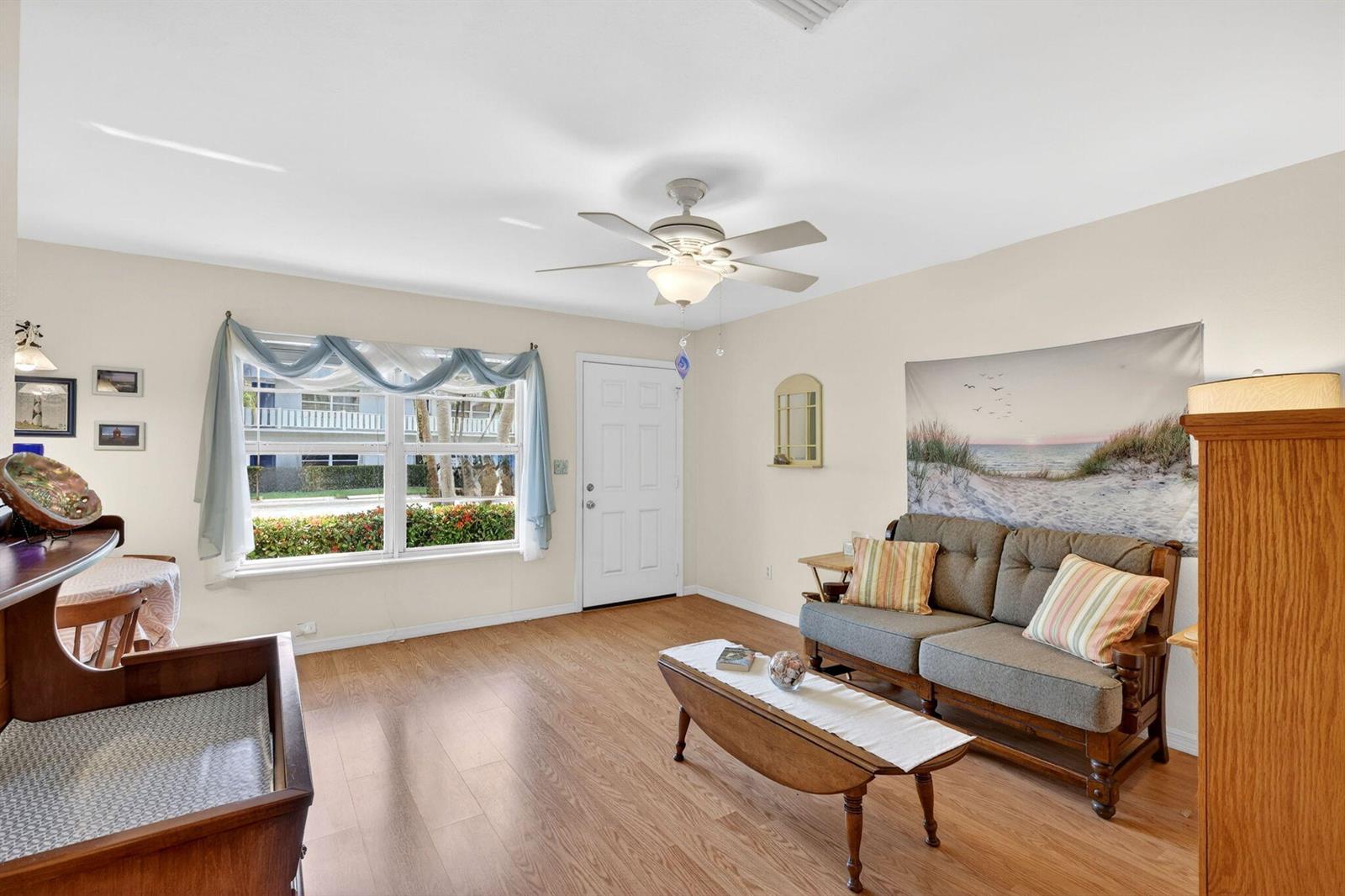 A living room features wood-look flooring, a ceiling fan, a sofa, and a large window — 2929 SE Ocean Boulevard # M4, Stuart FL 34996, STUART, FL