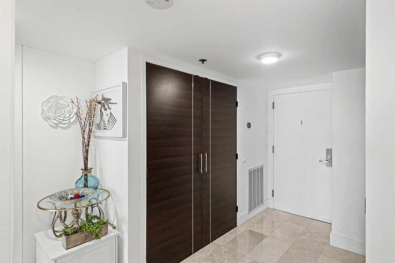 An entryway features a white door, dark wood-paneled closet doors, and a small decorative table — 901 E Camino Real # 1c, Boca Raton FL 33432, BOCA RATON, FL